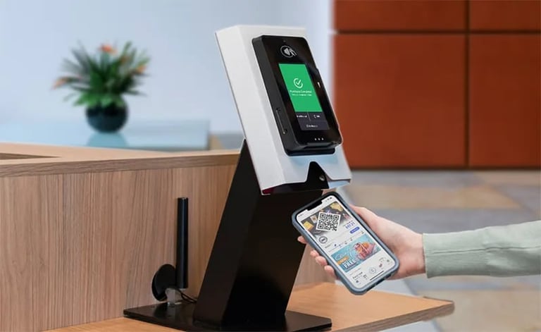 Person holding smartphone at contactless payment terminal in modern office setting with wooden desk and green plant